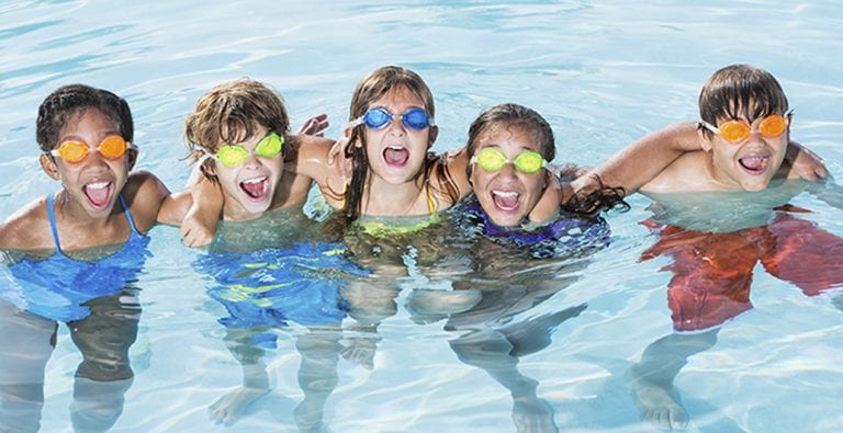 children with goggles in pool smiling
